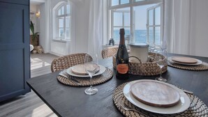 Un coin repas avec vue sur la mer, une bouteille de champagne et des paniers en osier sur la table.
