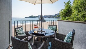 Un balcon agrémenté de meubles en osier, une table avec des boissons et des verres, et une vue sur la plage et l’océan.