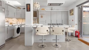 Uma cozinha moderna com ilha central, banquetas, máquina de lavar e uma janela grande.