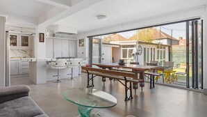 Cozinha moderna com armários brancos, área de jantar com mesa de vidro e vista para o quintal através de grandes portas de correr.