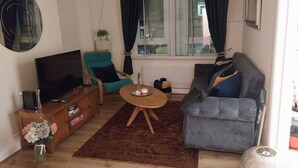 En stue med et fjernsyn, en turkis lænestol, en grå sofa, et træ sofabord og en brun måtte.