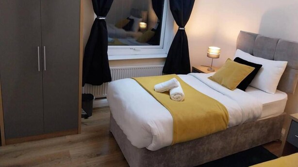 Et hotelværelse med seng, skab, et vindue med gardiner, en sengebordlampe og en radiator.