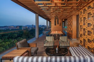 Un balcón amplio con techo de madera, un rincón de comedor con sillas a rayas y vistas a la ciudad.
