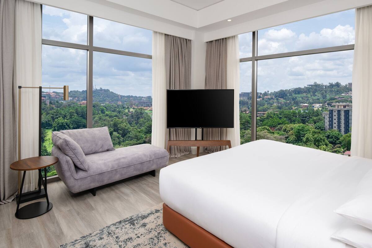 A hotel room with a large bed, a sofa, a TV, and a view of a cityscape.