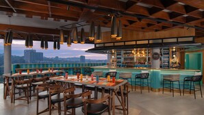 Un restaurante con zona de bar, mesas y sillas de madera, y vistas a la ciudad.