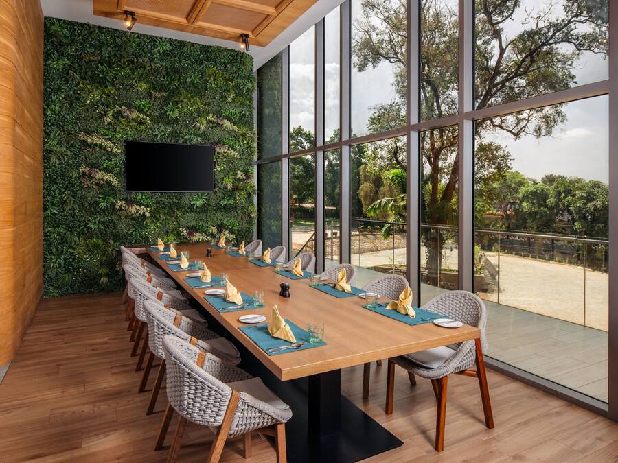Una larga mesa de comedor con sillas, un televisor de pantalla plana y una pared verde.