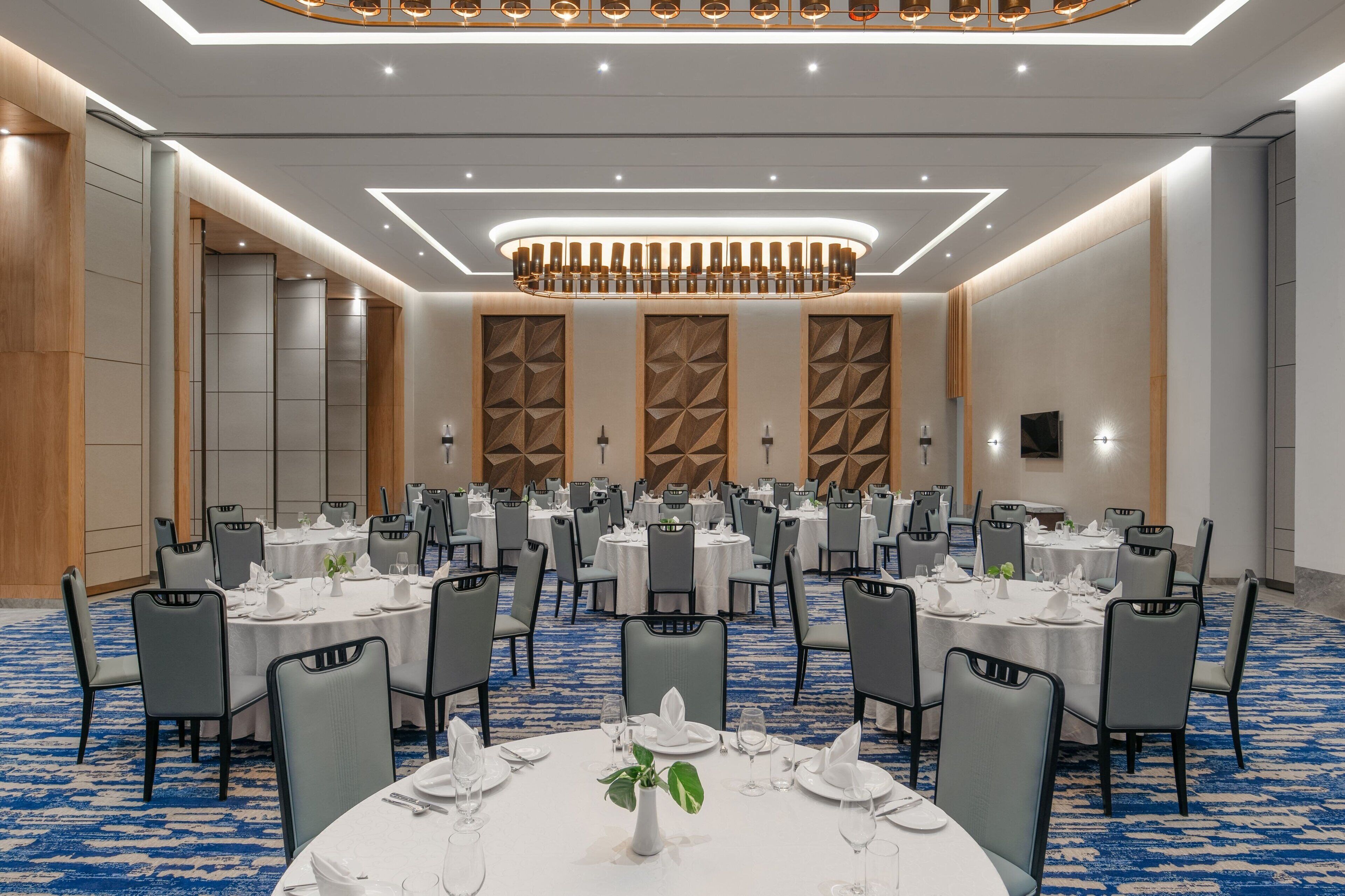 A banquet hall with round tables, grey chairs, and a blue carpet.