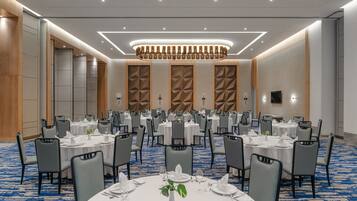 A banquet hall with round tables, grey chairs, and a blue carpet.