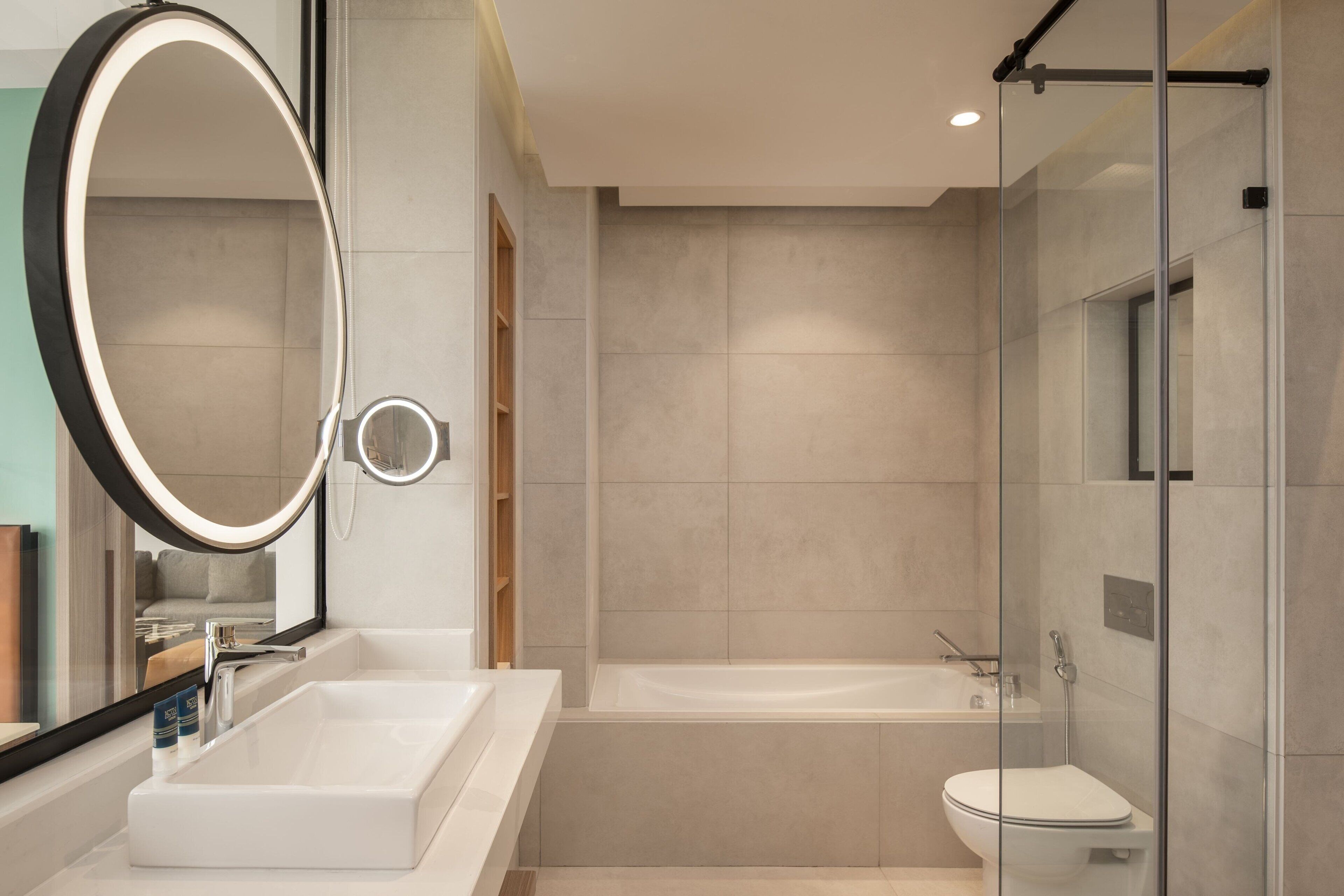 A modern bathroom with a large oval mirror, a rectangular sink, a bathtub, and a glass-enclosed shower area.