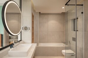 Un baño moderno con un espejo ovalado grande, un lavamanos rectangular, una bañera y una zona de ducha con mampara de cristal.