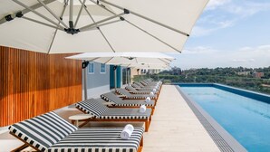 Un área de piscina en la azotea con sillones de descanso y sombrillas, paneles de madera y vistas a la ciudad.