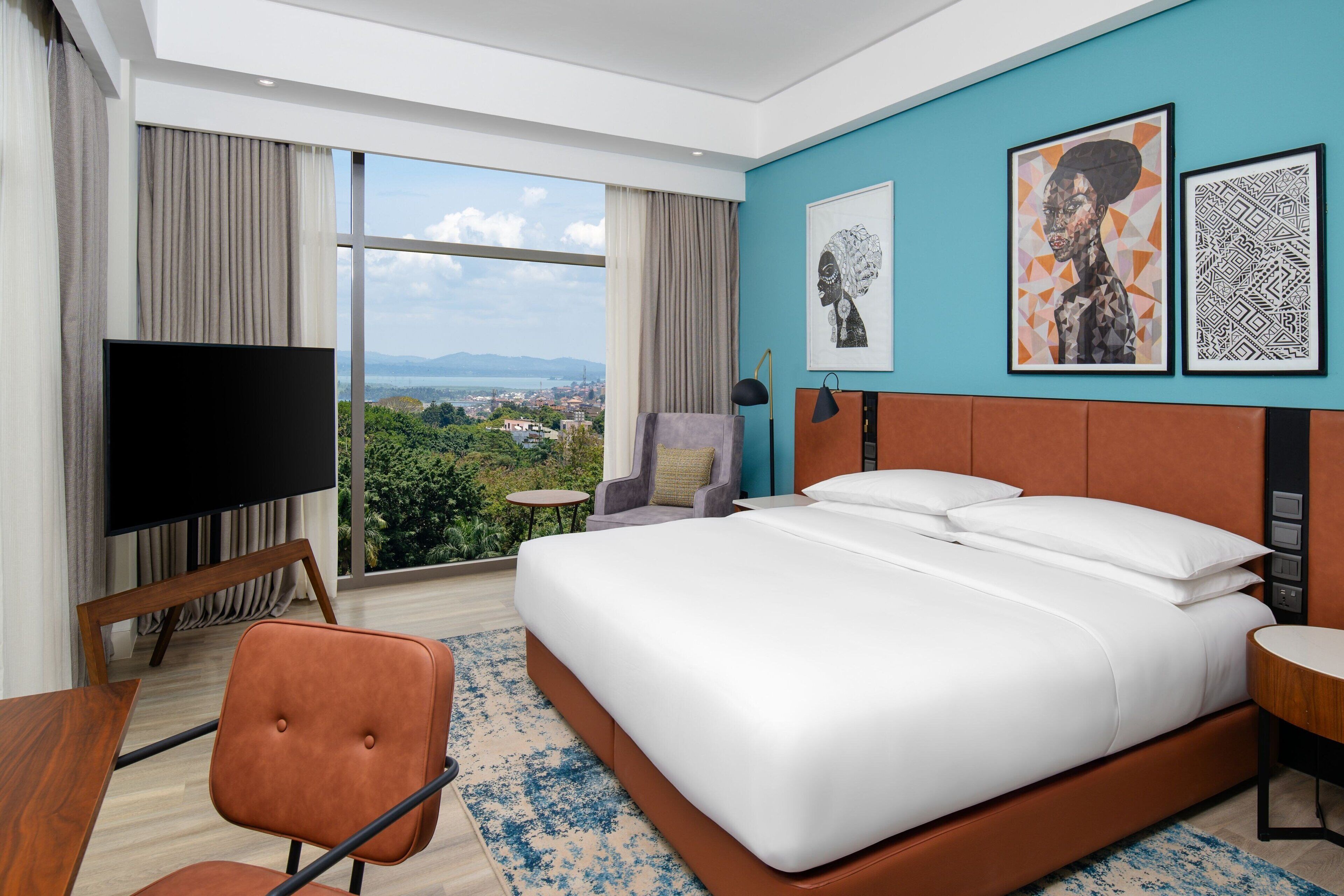 A hotel room with a large bed, a TV, a chair, and a view of the city.