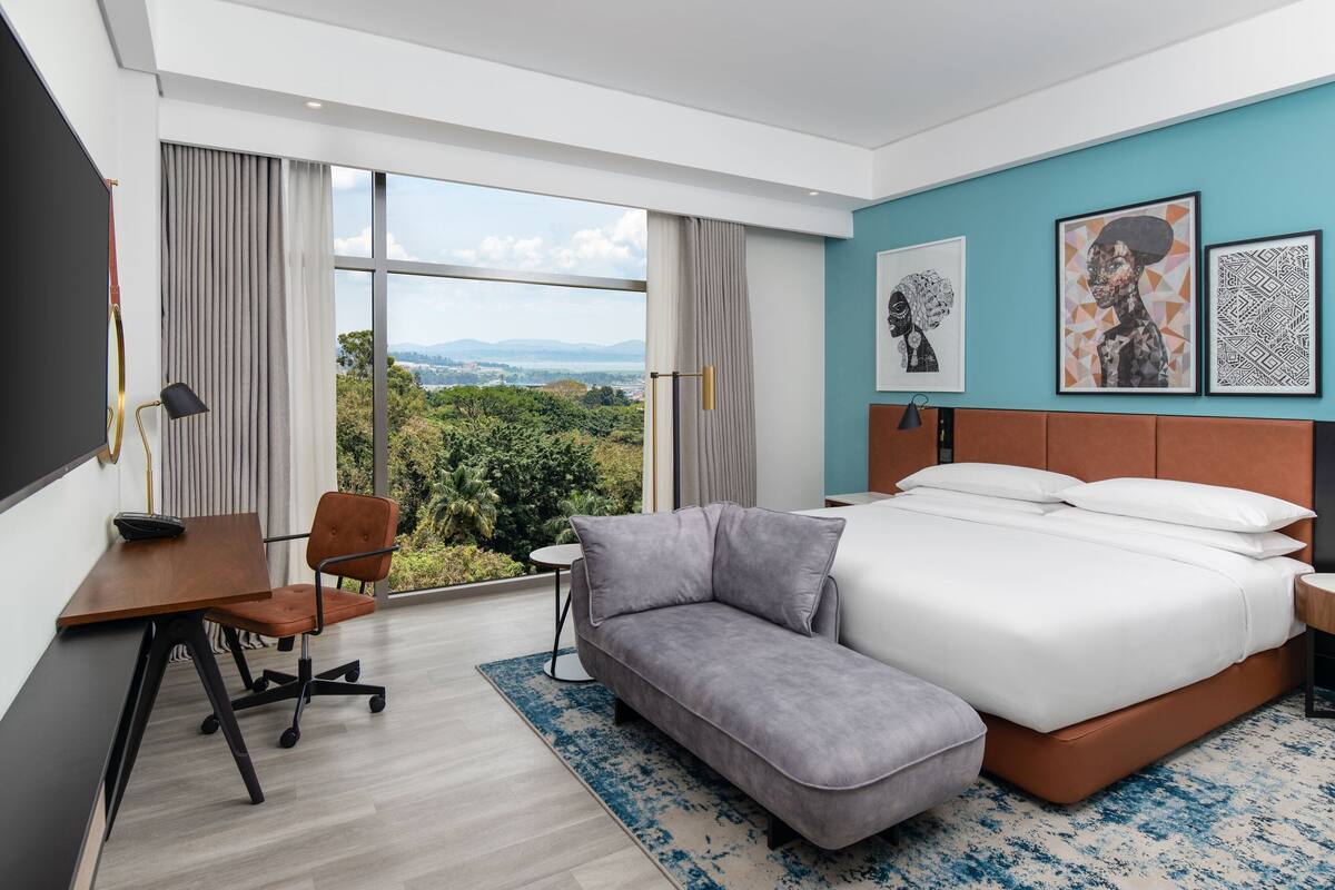 A modern hotel room with a large bed, a desk, and a view of the outdoors.