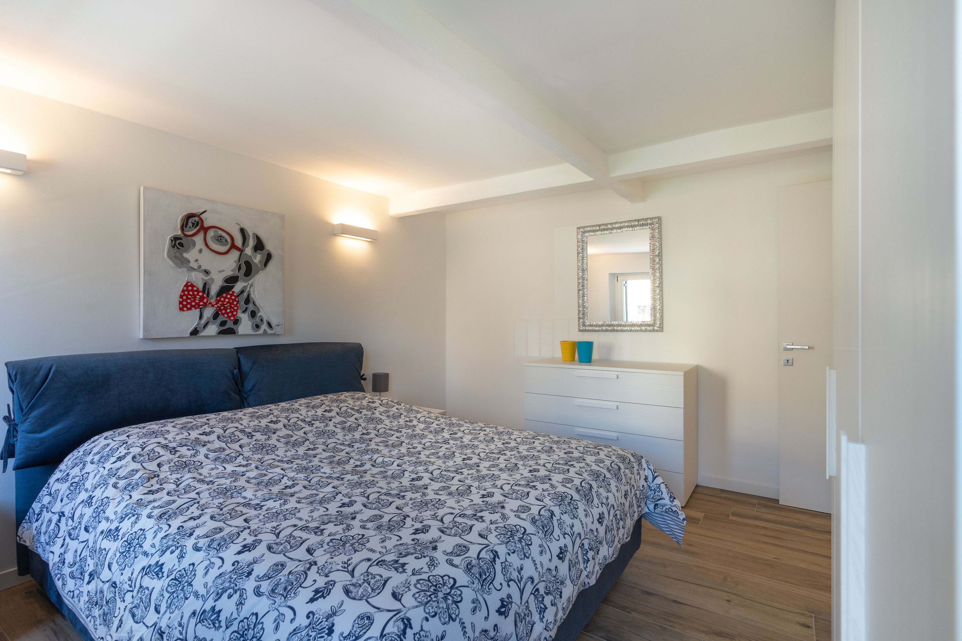 A bedroom with a bed, a dresser, a mirror, and a wall art piece.