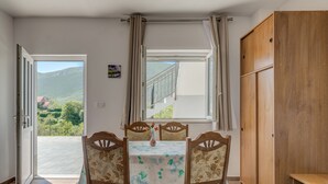 A room with a dining table and chairs, a wooden wardrobe, and a window with a view of greenery and hills. - Vacation House With the Pool, Near River Cetina (Omis)