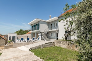 A modern two-story house with a balcony, a staircase, and a pool area with lounge chairs.