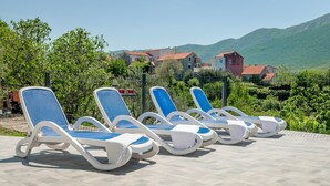A row of sun loungers on a tiled patio with a view of houses and hills in the background. - Vacation House With the Pool, Near River Cetina (Omis)