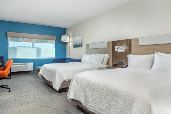 Une chambre d’hôtel avec deux lits, un bureau, une chaise orange et une fenêtre avec des stores.
