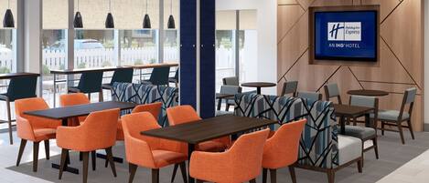A hotel lobby with modern furniture, a large TV screen, and large windows offering views of the outside.