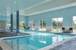 Una piscina interior con agua azul cristalina, rodeada de paredes con amplios ventanales y suelo de baldosas.