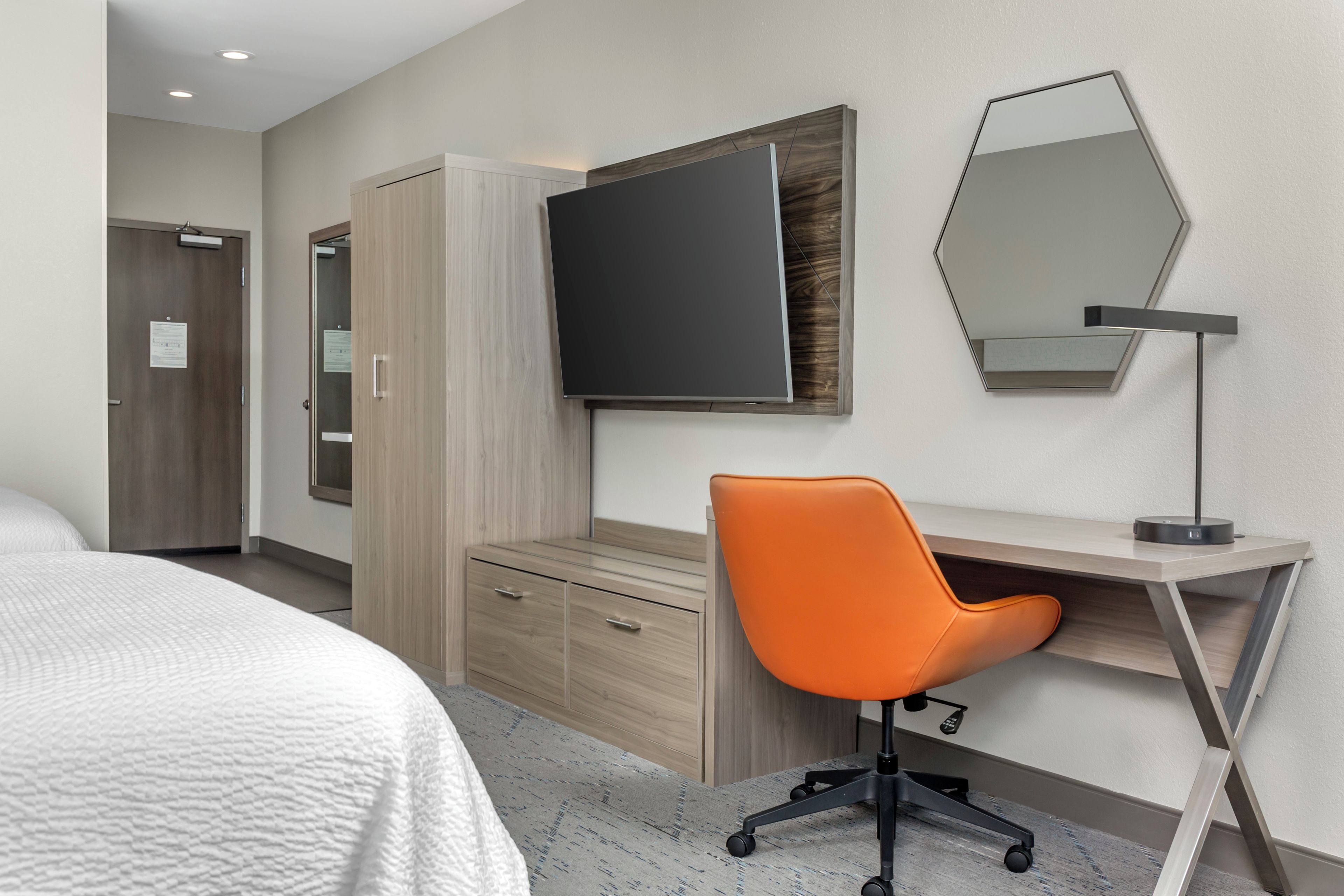 Une chambre d’hôtel comprenant un lit, un bureau avec une chaise, un téléviseur à écran plat, un miroir et une armoire.