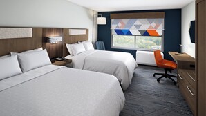 A hotel room with two beds, a desk, a chair, and a window with a view.