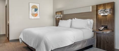 A modern hotel room with a large bed, a bedside table with a phone, and a wall-mounted light fixture.