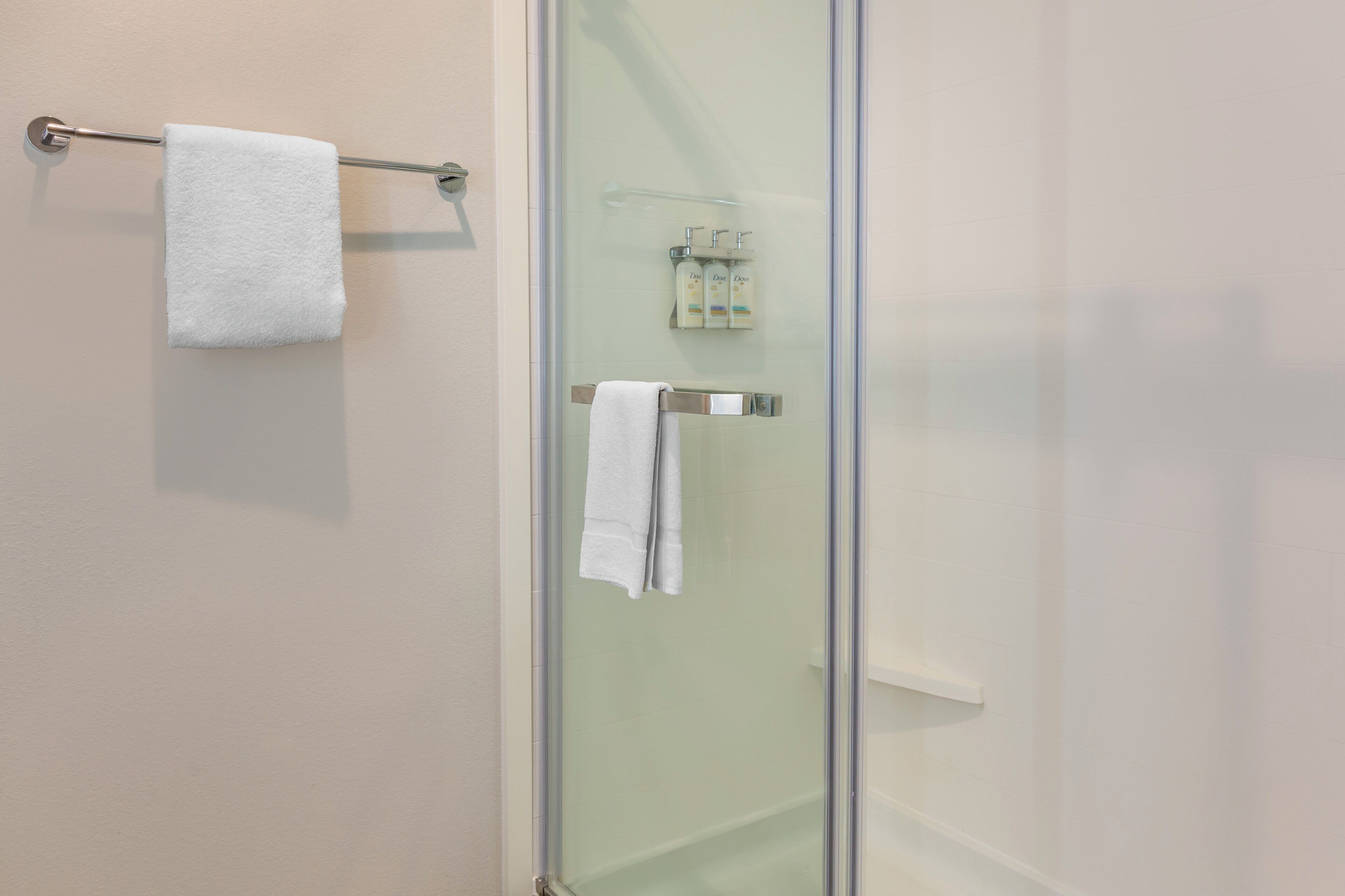 Un baño con cabina de ducha de vidrio, un perchero con una toalla blanca y un dispensador de jabón.
