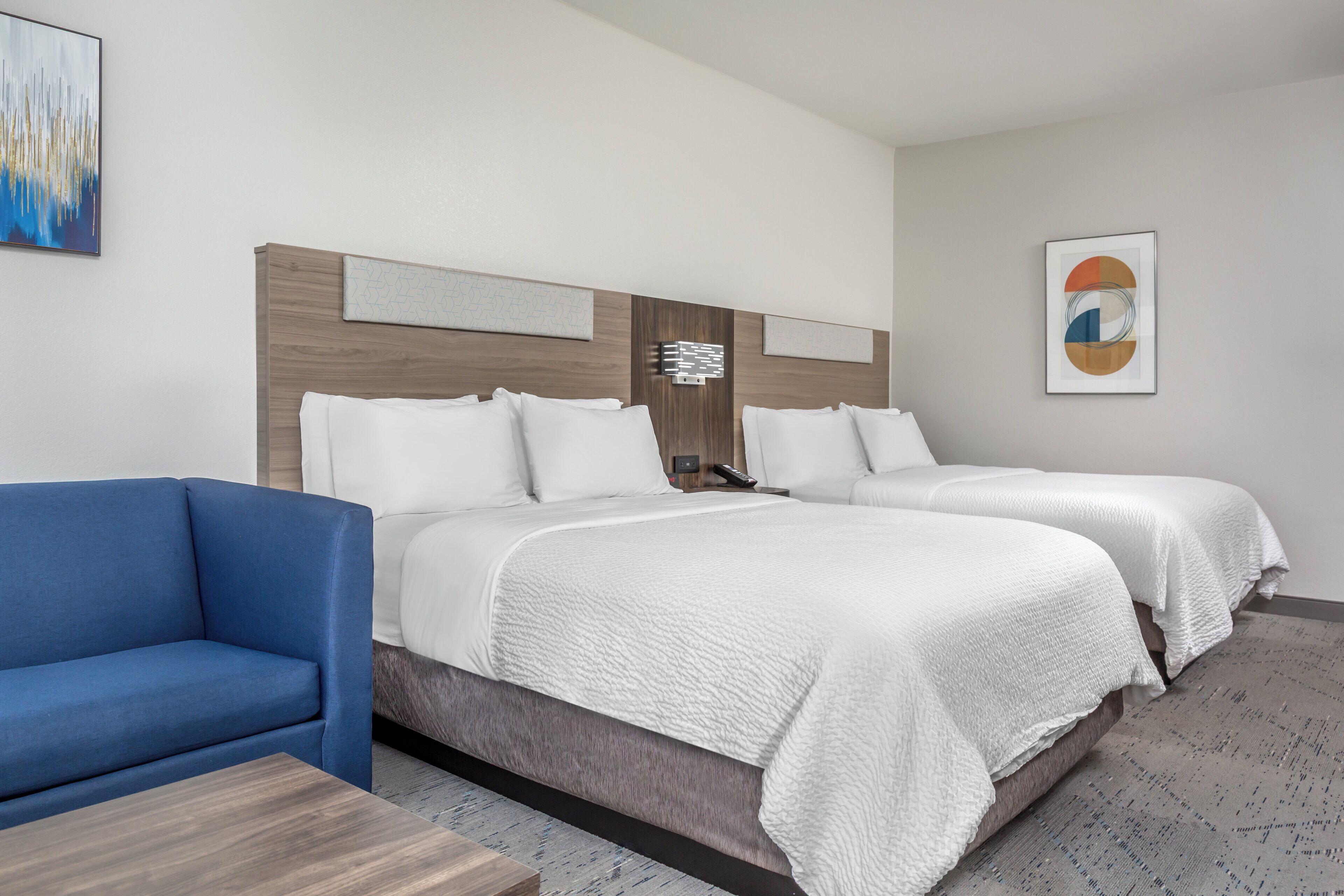 Une chambre d’hôtel avec deux lits, un canapé bleu et des œuvres d’art accrochées aux murs.