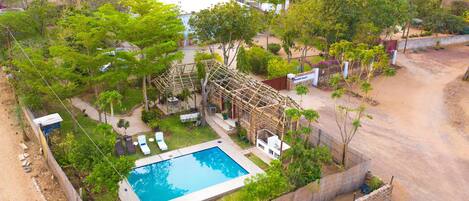 An aerial view of a property with a swimming pool, outdoor seating, and a wooden pergola.
