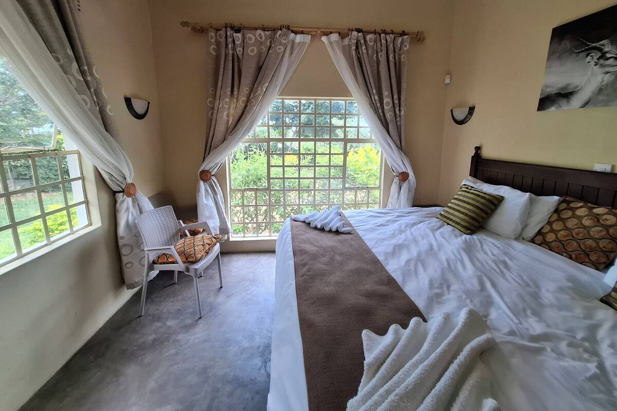 Une chambre d’hôtel avec un lit, une chaise, une fenêtre avec des rideaux et une vue sur la verdure.