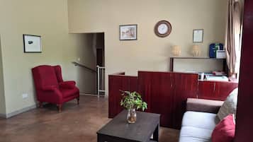 A living room with a red armchair, a grey sofa, a wooden reception desk, and a staircase leading to another room.
