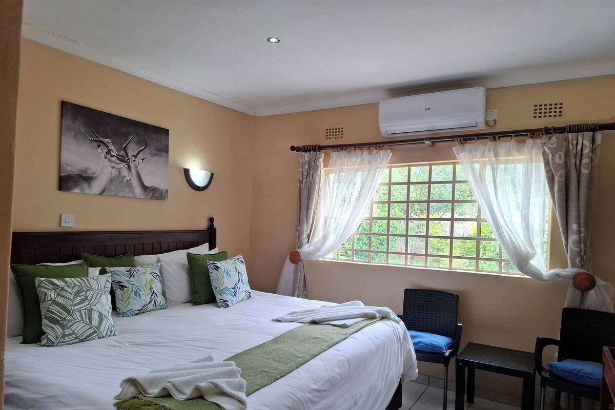 Une chambre d’hôtel comprenant un lit, une chaise, une fenêtre avec des rideaux, un appareil de climatisation et un luminaire fixé au mur.