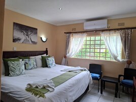 Une chambre d’hôtel comprenant un lit, une chaise, une fenêtre avec des rideaux, un appareil de climatisation et un luminaire fixé au mur.