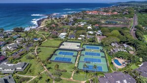 Vista aerea di una zona residenziale costiera con campi da tennis, case e una spiaggia.