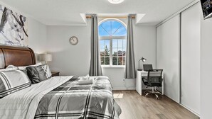 Un dormitorio con cama, escritorio, silla, reloj y ventana con cortinas.