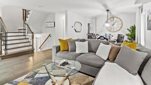 Una sala de estar moderna con un sofá seccional gris, una mesa de centro de vidrio y una escalera con barandillas de madera.