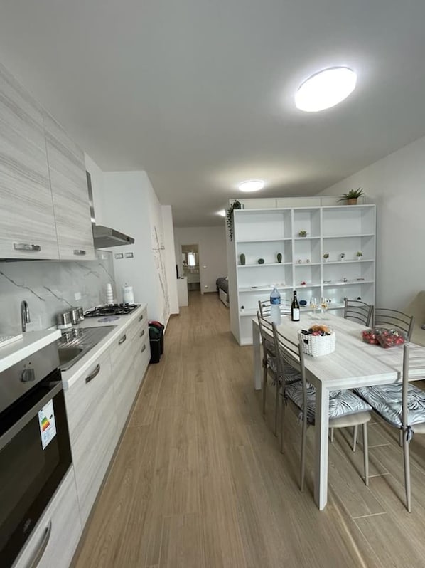 A modern kitchen with white cabinetry, a built-in oven, and a dining area with a white table and metal chairs.