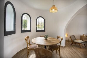 A dining area with a round wooden table, four wicker chairs, and two arched windows with metal grilles.