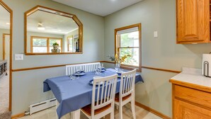A dining area with a table set for two, a mirror above the table, and a window with a view of greenery. - Dog-Friendly Watertown Vacation Rental w/ Deck (Watertown)