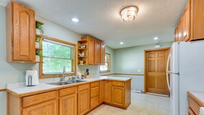 A kitchen with wooden cabinets, a white refrigerator, a sink, and a window with blinds. - Dog-Friendly Watertown Vacation Rental w/ Deck (Watertown)