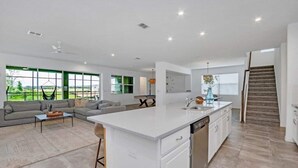A modern open-plan living area with a kitchen island, dining table, and a staircase leading to an upper level.