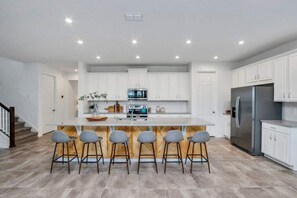 Une cuisine moderne avec des meubles blancs, un îlot central doté de tabourets, des appareils en acier inoxydable et un plancher en bois.