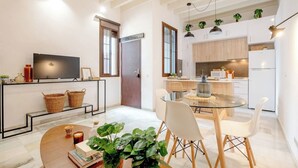 A modern kitchen with white cabinets, a dining area with a glass table and white chairs, and a TV on the wall. - Home2Book Amelia's Pottery, Triana (Sevilla)