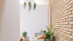 A cozy living area with a brick wall, a wooden ceiling, and a sofa with cushions. There are potted plants and a small table with a rug. - Home2Book Amelia's Pottery, Triana (Sevilla)