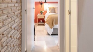 A narrow hallway leading to a bedroom with a brick wall, a bedside table with a lamp, and a bed with a headboard. - Home2Book Amelia's Pottery, Triana (Sevilla)