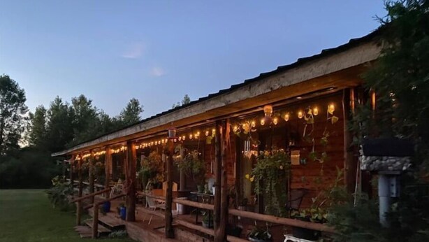 Una cabaña de madera con un porche cubierto, que incluye asientos exteriores y luces colgantes.