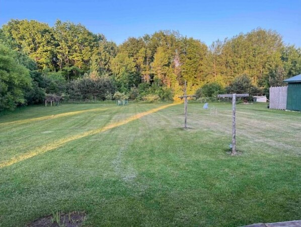 A well-maintained grassy yard with a wooden fence, a small shed, and dense trees in the background. - Log Cabin house on 10.5 acers of wooded land. Accommodates 20 plus guest. (Remus)