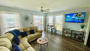 A living room with a beige sectional sofa, a round coffee table, and a TV on the wall. - Cherry Grove 2 bedroom condo, just a block off the beach.  (North Myrtle Beach)