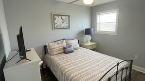 A bedroom with a bed, a desk, a ceiling fan, a window, and a wall-mounted artwork. - Cherry Grove 2 bedroom condo, just a block off the beach.  (North Myrtle Beach)